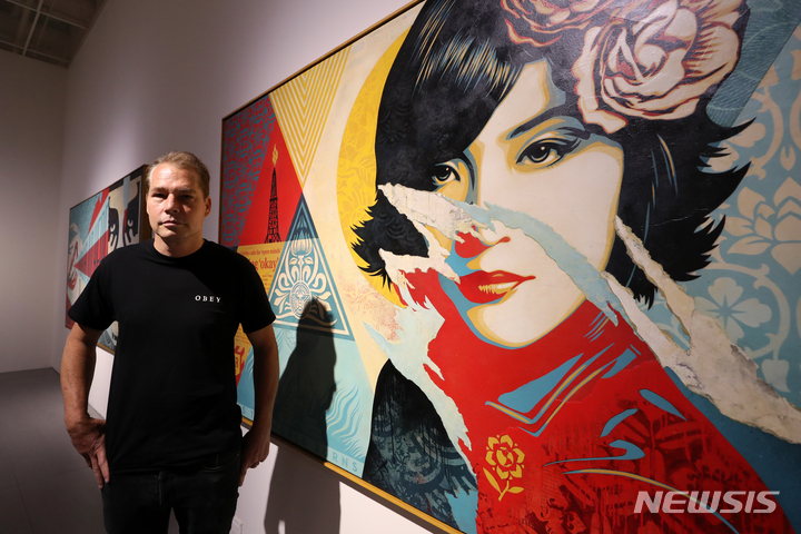 [서울=뉴시스] 박진희 기자 = 셰퍼드 페어리(Shepard Fairey)가 28일 서울 송파구 롯데뮤지엄에서 열린 기획전 '셰퍼드 페어리, 행동하라! EYES OPEN, MIND OPEN' 전시 작품 '오프 마인즈' 앞에서 사진 촬영을 하고 있다. 작품 '오픈 마인즈'는 물, 화학제품, 모래 등을 혼합한 물질을 고압으로 분사해 바위를 파쇄하여 석유와 가스를 분리하는 기술인 수압 파쇄법의 이중성에 대해 이야기 한다. 2022.07.28. pak7130@newsis.com