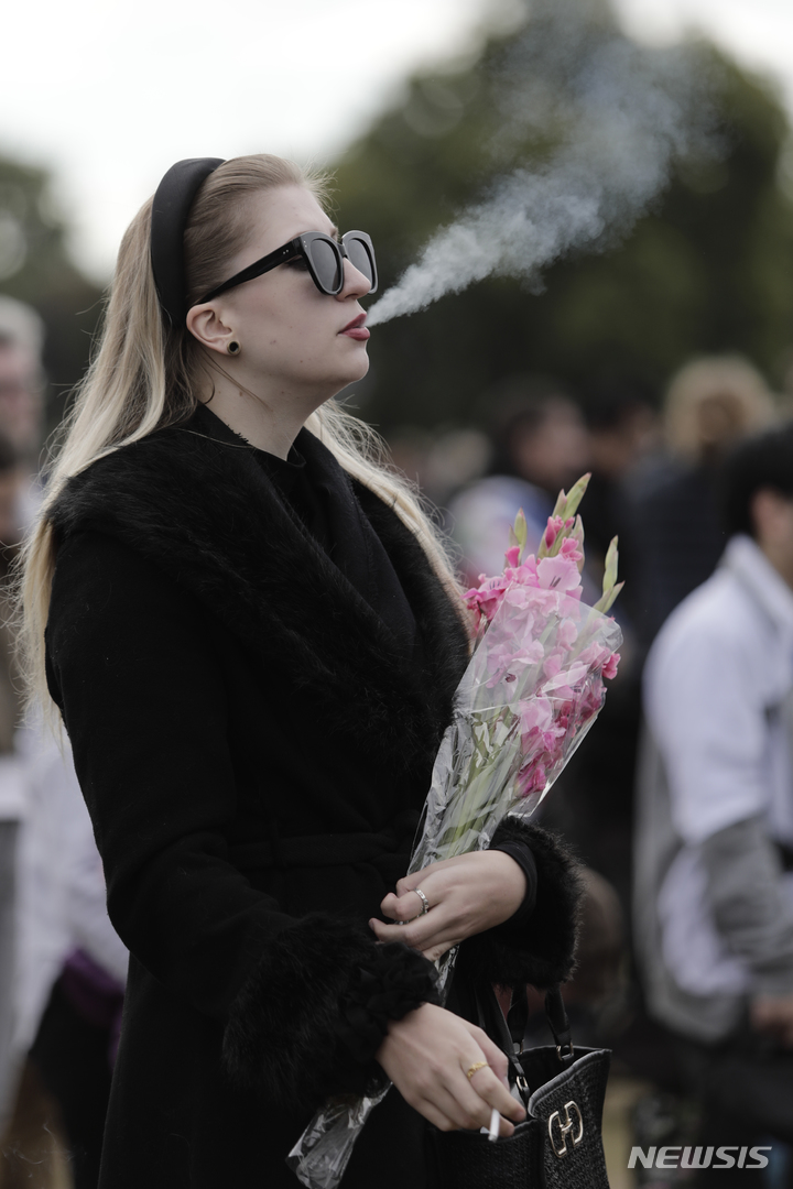[런던=AP/뉴시스] 19일(현지시간) 영국 런던의 하이드파크에서 고 엘리자베스 2세 영국 여왕의 장례식을 대형 스크린으로 지켜보던 한 여성이 담배 연기를 내뿜고 있다. 2022.09.19.