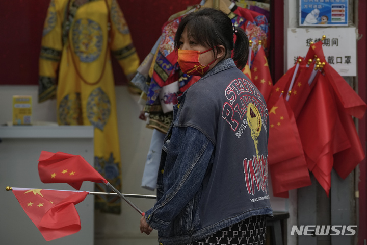 [베이징=AP/뉴시스] 마스크를 착용한 한 점원이 2일, 일주일 간의 국경절 연휴기간에 자금성 근처 상점에서 판매되는 중국 국기를 흔들고 있다. 2022.10.04.