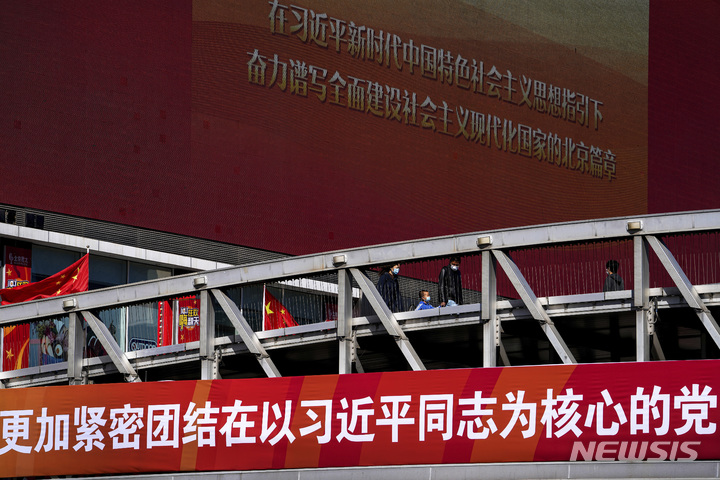 [베이징=AP/뉴시스]2022년 10월4일 중국 수도 베이징의 한 쇼핑가에서 안면마스크를 쓴 한 가족이 정부 선전 메시지를 보여주는 거대한 스크린을 배경으로 보행자 다리를 따라 걷고 있다.2023.01.03.