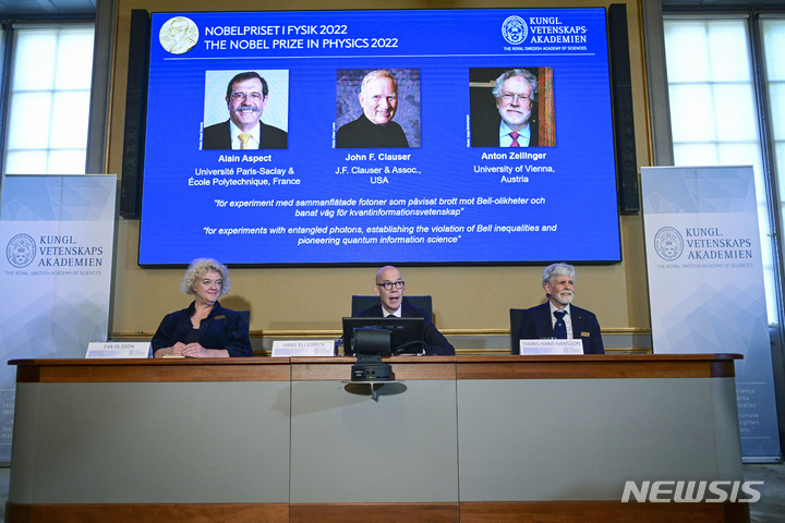 [스톡홀름(스웨덴)=AP/뉴시스]스웨덴 왕립과학원의 한스 엘레그렌 사무총장(가운데)과 노벨 물리학위원회의 에바 올슨(왼쪽), 토르스 한스 핸슨 위원이 4일 스톡홀름에서 2022년 노벨 물리학상 수상자를 발표하고 있다. 이들의 머리 위 화면에 알랭 아스펙트(프랑스), 존 클로저(미), 안톤 자일링거(오스트리아, 왼쪽부터) 등 공동수상자 3명의 사진이 보인다. 2022.10.4 
