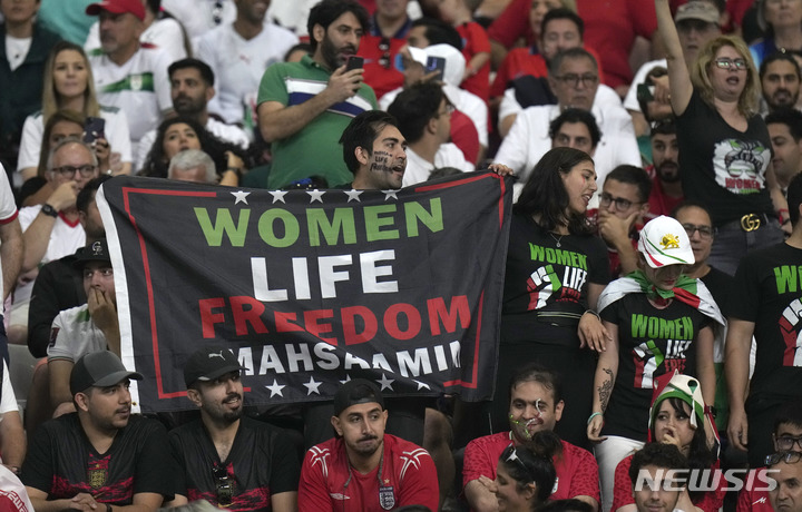 [도하=AP/뉴시스] 이란 축구팬들이 21일(한국시간) 카타르 도하의 칼리파 국제경기장에서 열린 잉글랜드와 2022 FIFA 카타르 월드컵 B조 첫 경기 도중 마샤 아미니의 죽음을 기리며 '여성, 생명, 자유'라는 문구가 적힌 팻말을 들고 있다. 2022.11.21.