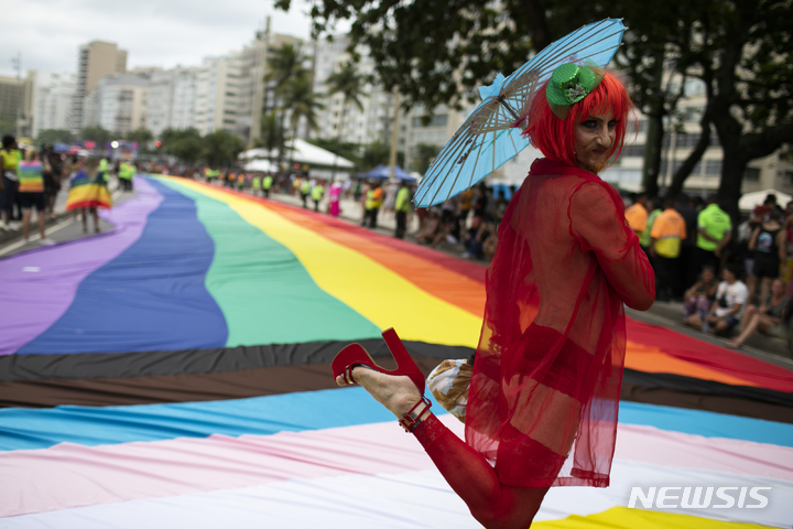 [리우데자네이루=AP/뉴시스] 27일(현지시간) 브라질 리우데자네이루 코파카바나 해변에서 제27회 게이 프라이드 퍼레이드(Gay Pride Parade)가 열려 한 참가자가 대형 무지개 깃발 앞에서 점프샷을 찍고 있다. 2022.11.28.
