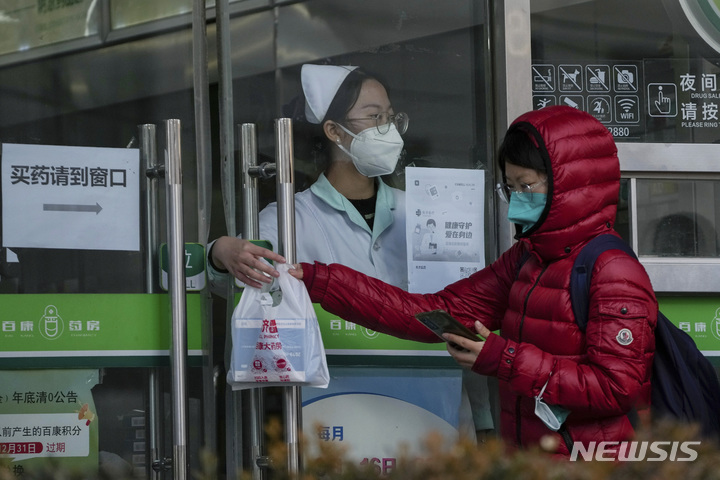 [베이징=AP/뉴시스] 11일 중국 베이징의 한 약국에서 약국 직원이 문틈으로 고객에게 약품을 전달하고 있다. 2022.12.12