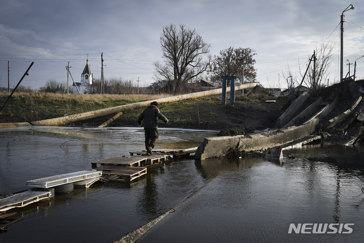 [바흐무트=AP/뉴시스] 11일(현지시간) 우크라이나 도네츠크주 바흐무트에서 한 주민이 러시아군과의 전투로 파괴된 다리에 놓인 임시 다리로 강을 건너고 있다. 2022.12.12.