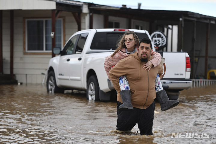 [브렌트우드=AP/뉴시스] 16일(현지시간) 미 캘리포니아주 브렌트우드에서 한 남성이 아내를 업어 물에 잠긴 집에서 대피시키고 있다. 캘리포니아에 3일간 폭우가 이어지면서 날씨가 추워져 일부 지역에는 한파주의보가 발령됐다. 2023.01.17.