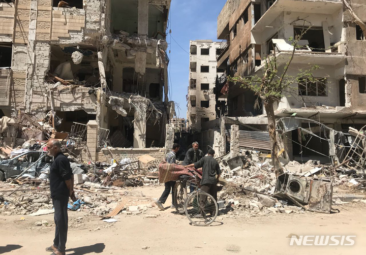 [두마(시리아)=AP/뉴시스]지난 2018년 4월16일 정부군의 화학무기 공격을 받은 것으로 의심되는 시리아 다마스쿠스 인근 두마 마을의 파손된 건물 앞에 사람들이 서 있다. 세계화학무기금지기구(OPCW)는 27일 시리아 공군이 지난 2018년 4월 시리아 두마에 염소가스가 든 실린더 2개를 떨어뜨려 43명이 사망했다는 '합리적인 근거'가 있다는 조사 결과를 내놓았다. 2023.1.27