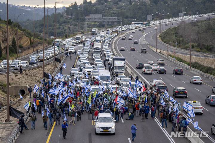 [텔아비브=AP/뉴시스] 9일(현지시간) 이스라엘 텔아비브에서 예비군들이 도로를 막고 국기를 흔들며 베냐민 네타냐후 총리 연립 정부의 사법 개혁 추진에 반대하는 시위를 벌이고 있다. 2023.02.10.