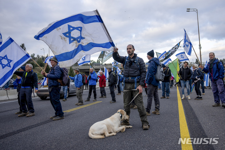 [텔아비브=AP/뉴시스] 9일(현지시간) 이스라엘 텔아비브에서 예비군들이 도로를 막고 국기를 흔들며 베냐민 네타냐후 총리 연립 정부의 사법 개혁 추진에 반대하는 시위를 벌이고 있다. 2023.02.10.