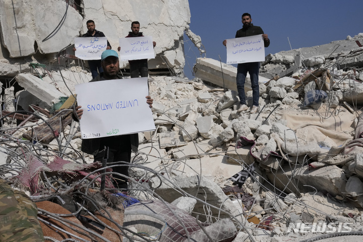 [아타렙=AP/뉴시스] 12일(현지시간) 시리아 아타렙에서 지진 피해 주민들이 유엔에 항의하는 손팻말을 들고 파괴된 집 잔해에 서서 시위하고 있다. 2023.02.13.