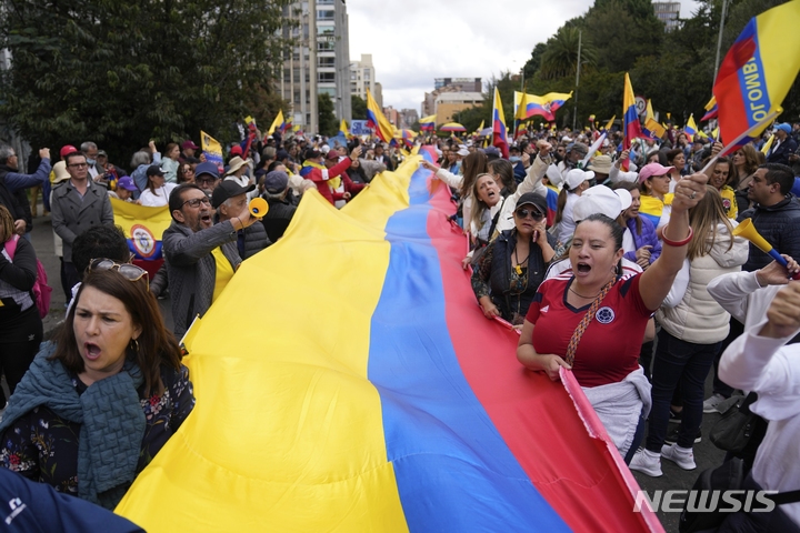 [보고타=AP/뉴시스] 15일(현지시간) 콜롬비아 보고타에서 구스타보 페트로 대통령의 의료보험 개혁안 등에 반대하는 시위대가 대형 국기를 들고 구호를 외치고 있다. 우파 야당이 주도한 이날 시위는 페트로 대통령 지지자들의 개혁안 찬성 시위 하루 만에 열렸다. 2023.02.16.