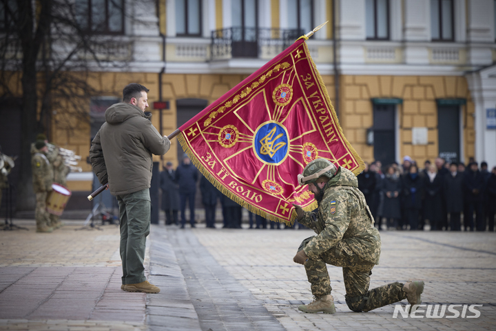 [키이우=AP/뉴시스] 볼로디미르 젤렌스키(왼쪽) 우크라이나 대통령이 24일(현지시간) 키이우에서 러시아의 우크라이나 침공 1년을 맞아 열린 행사에 참석해 군부대 깃발을 들고 있는 동안 한 장교가 깃발에 입 맞추고 있다. 2023.02.24.