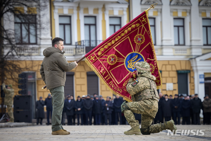 [키이우(우크라이나)=AP/뉴시스]우크라이나 수도 키이우에서 24일 전쟁 발발 1주년을 맞아 열린 기념행사에서 볼로디미르 젤렌스키 우크라이나 대통령이 들고 있는 우크라이나군 군기에 한 우크라이나군 장교가 무릎을 꿇고 입맞추고 있다. 젤렌스키 대통령은 이날 "러시아가 우크라이나를 침공한 2022년 2월24일은 우리 생애에서 가장 긴 날"이라고 24일 말했다. 2023.2.24