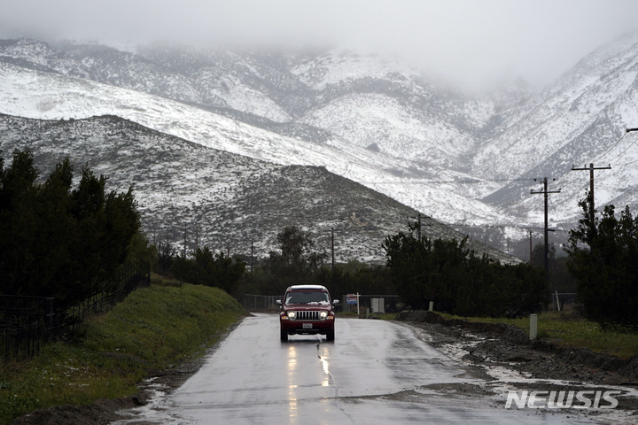 [캘리포니아=AP/뉴시스] 운전자가 24일(현지시간) 캘리포니아 아구아 둘체의 눈 덮힌 언덕을 뒤로하며 젖은 도로 위를 달리고 있다. 최근 미국을 강타한 겨울폭풍으로 캘리포니아와 서부 지역 일대에 폭설과 비가 내렸다. 2023.02.27.