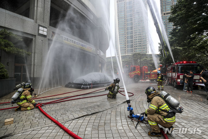 [서울=뉴시스] 정병혁 기자 = 14일 서울 강남구 타워팰리스에서 열린 전기차 화재 대비 초고층 건축물 민간 자율주도 소방훈련에서 소방 관계자들이 굴절차에 설치된 하강구조대를 사용해 고층에 있는 시민을 구조한 뒤 건물을 향해 물을 뿌리고 있다. 2023.06.14. jhope@newsis.com