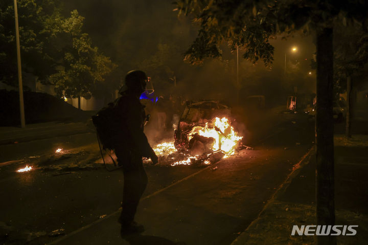 [낭테르=AP/뉴시스] 30일(현지시간) 프랑스 파리 교외 낭테르에서 경찰이 교통검문 중 17세 배달기사를 사살한 것에 분노한 시위대가 시위를 벌인 가운데 경찰이 불에 탄 차량을 바라보고 있다. 2023.06.30.