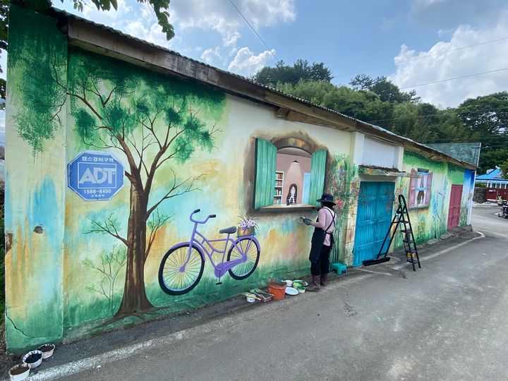 [고성(경남)=뉴시스] 신정철 기자= 경남 고성군 영현면(면장 장혜정)이 펼치는 재능나눔 릴레이 사업이 면민들의 반김속에 탄력을 받고 있다. 지난 3월 8일 제1탄 이연숙·김순선 씨의 옷수선 봉사에 이어 제2탄 사업으로 마을창고 벽화사업을 펼쳤다. 사진은 지난 28일 마을 초입의 낡고 오랫동안 방치된 창고에 벽화를 칠하고 있다.(사진=고성군 제공).2023.06.30. photo@newsis.com *재판매 및 DB 금지