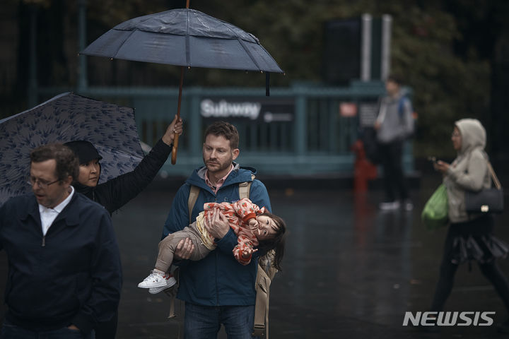[뉴욕=AP/뉴시스] 29일(현지시각) 미국 뉴욕에서 한 여성이 아이를 안고 있는 남편에게 우산을 받쳐주고 있다. 뉴욕 일대에 전날 밤부터 폭우가 쏟아져 일부 지하철과 통근 열차 운행이 중단돼 출근길 시민들이 대란을 겪었다. 2023.09.30.