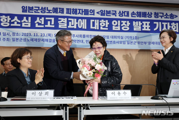 [서울=뉴시스] 조성우 기자 = 일본군 위안부 피해자들이 일본 정부를 상대로 낸 손해배상 청구 소송 항소심에서 법원이 1심을 뒤집고 일본국이 피해자들에게 위자료를 지급해야 한다고 23일 판단 내린데 대해, 일본 언론들은 신속하게 타전했다. 사진은 일본군 위안부 피해자 이용수 할머니가 23일 오후 서울 서초구 민주사회를 위한 변호사모임 대회의실에서 열린 일본 상대 손해배상 청구 소송 항소심 1심 패소 취소 판결 결과에 대한 입장 발표 기자회견에서 조용선 민변 회장으로부터 꽃다발을 받고 있는 모습. 이상희 민변 일본군위안부문제대응TF 단장(앞줄 왼쪽부터), 조용선 민변 회장, 이용수 할머니, 이나영 정의기억연대 이사장.2023.11.23. xconfind@newsis.com