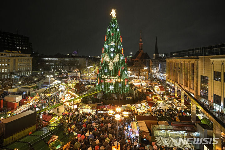 [도르트문트=AP/뉴시스] 27일(현지시각) 독일 도르트문트의 비 내리는 크리스마스마켓에서 시민들이 45m 높이의 전통 크리스마스트리를 구경하고 있다. 도르트문트시는 이 트리가 1000여 그루의 가문비나무로 만들어지고 약 5만 개의 조명과 장신구가 달린 세계 최대 크리스마스트리 중 하나라고 밝혔다. 2023.11.28.
