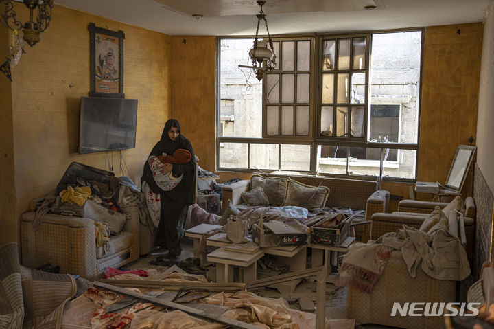 [라파=AP/뉴시스] 가자지구 라파에서 9일(현지시간) 한 팔레스타인 여성이 이스라엘 폭력 영향을 받은 건물에서 아기를 안고 있는 모습. 2023.12.10.