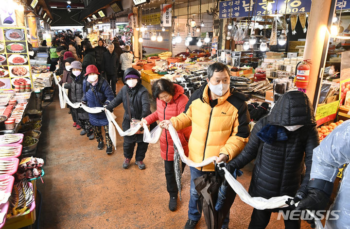 [수원=뉴시스] 김종택 기자 = 17일 경기도 수원시 팔달구 못골시장에서 열린 '못골시장과 함께하는 가래떡 나눔 행사'에 참석한 시장상인과 시민들이 180m 길이의 가래떡을 이어 잡는 퍼포먼스를 하고 있다. 새해를 맞아 무병장수를 기원하며 긴 가래떡을 뽑는 가래떡 나눔은 못골시장의 대표 행사다. 2024.01.17. jtk@newsis.com