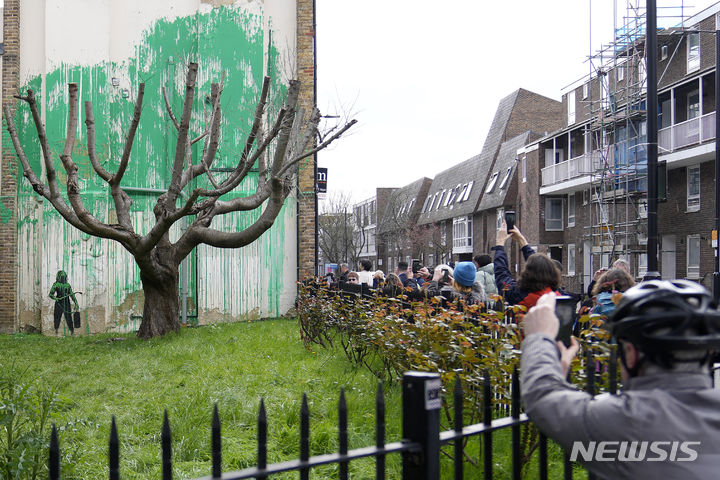 [런던=AP/뉴시스] 시민들이 18일(현지시각) 영국 런던 북부 핀스버러 공원 인근의 한 건물에 '얼굴 없는 화가'로 알려진 영국 유명 그라피티 작가 뱅크시가 그린 벽화를 보고 있다. 2024.03.19.