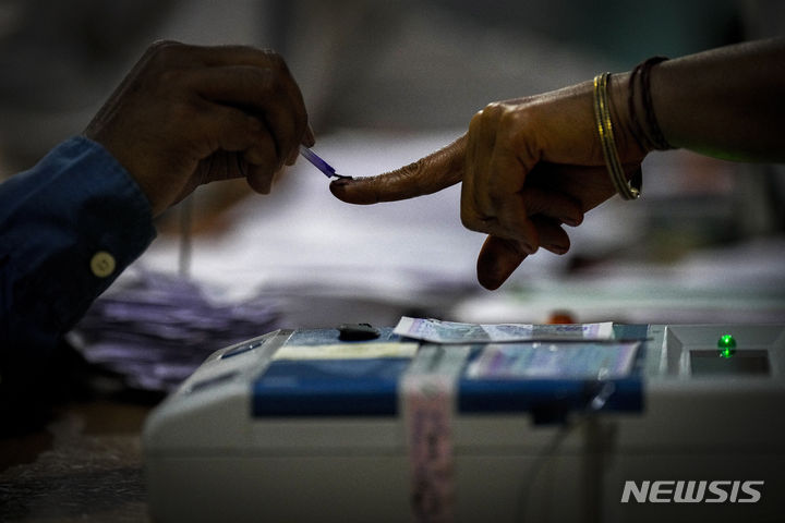 [아삼=AP/뉴시스] 19일 인도 아삼 북동부 조르하트주 바호나 마을에 마련된 인도 총선 투표소에서 투표소 관계자가 투표를 마친 유권자의 손에 잉크를 묻혀주고 있다. 2024.04.19.