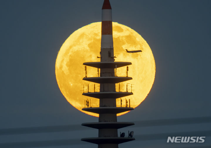 [프랑크푸르트=AP/뉴시스] 23일(현지시각) 독일 프랑크푸르트의 TV 송전탑 뒤로 보름달이 뜨는 동안 여객기 한 대가 지나가고 있다. 2024.04.24.