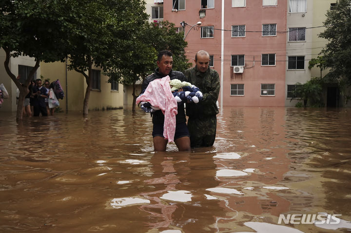 [리우그란데두술=AP/뉴시스] 4일(현지시각) 브라질 남부 리우그란데두술주 카노아스의 홍수 피해 지역에서 한 남성이 아기를 안은 채 대피하고 있다. 2024.05.07.