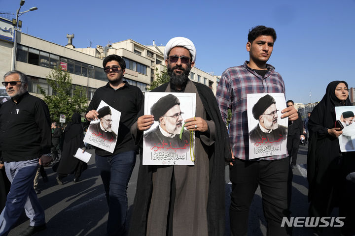 [테헤란=AP/뉴시스] 22일(현지시각) 이란 수도 테헤란에서 고 에브라힘 라이시 대통령과 헬기 추락 사고 희생자들의 장례식이 열려 추모객들이 라이시 대통령의 사진을 들고 운구행렬을 따르고 있다. 2024.05.22.