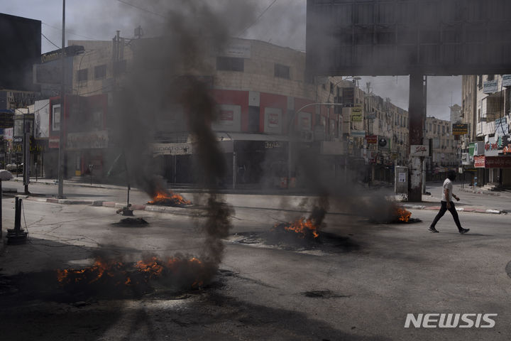 [제닌=AP/뉴시스] 5월 22일 요르단강 서안지구 제닌에서 팔레스타인 시위대와 이스라엘군이 충돌한 후 한 팔레스타인 남성이 타이어들이 불 타고 있는 거리를 지나고 있다. 2024.05.26.