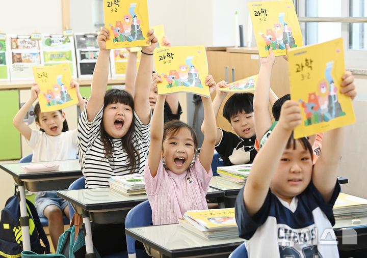 [수원=뉴시스] 김종택 기자 = 초등학교 개학이 시작된 19일 경기도 수원시 망포초등학교 3학년6반 학생들이 새학기 교과서를 들어보이며 즐거워하고 있다. 2024.08.19. jtk@newsis.com