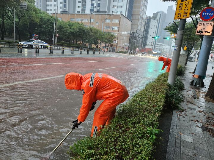 [부산=뉴시스] 권태완 기자 =호우경보가 발효된 21일 오전 부산 해운대구 중동의 한 도로가 집중호우로 물에 잠기자 소방대원들이 맨홀에서 쓰레기를 제거하는 등 안전 조치를 하고 있다. (사진=부산소방재난본부 제공) 2024.09.21. photo@newsis.com *재판매 및 DB 금지