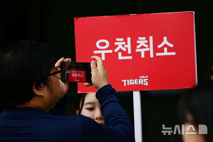 [광주=뉴시스] 이영주 기자 = 2024 KBO 포스트시즌 한국시리즈 KIA 타이거즈와 삼성 라이온즈의 1차전 서스펜디드 경기와 2차전이 우천 취소된 22일 오전 광주 북구 광주-기아챔피언스필드에서 한 시민이 경기장 관계자가 든 우천취소 팻말을 사진찍고 있다. 2024.10.22. leeyj2578@newsis.com