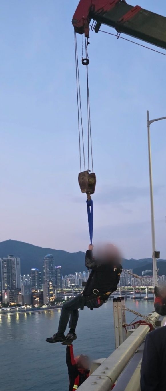 [부산=뉴시스] 11일 부산 광안대교 상판 난간에 들어가 고공시위를 벌인 A(50대)씨가 크레인으로 구조되고 있다. (사진=부산경찰청 제공) 2025.05.11. photo@newsis.com  *재판매 및 DB 금지